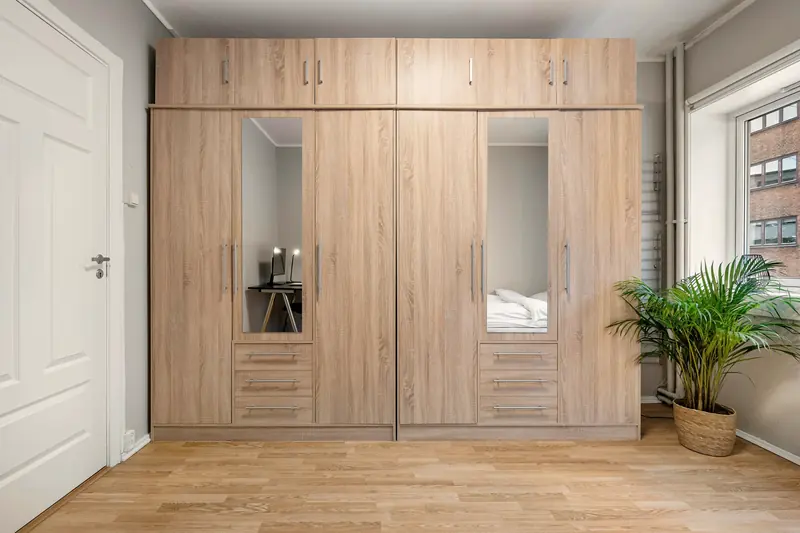 Raumhohe Schrankwand in heller Eiche mit zwei Spiegeltüren und Schubkästen in einem Schlafzimmer.