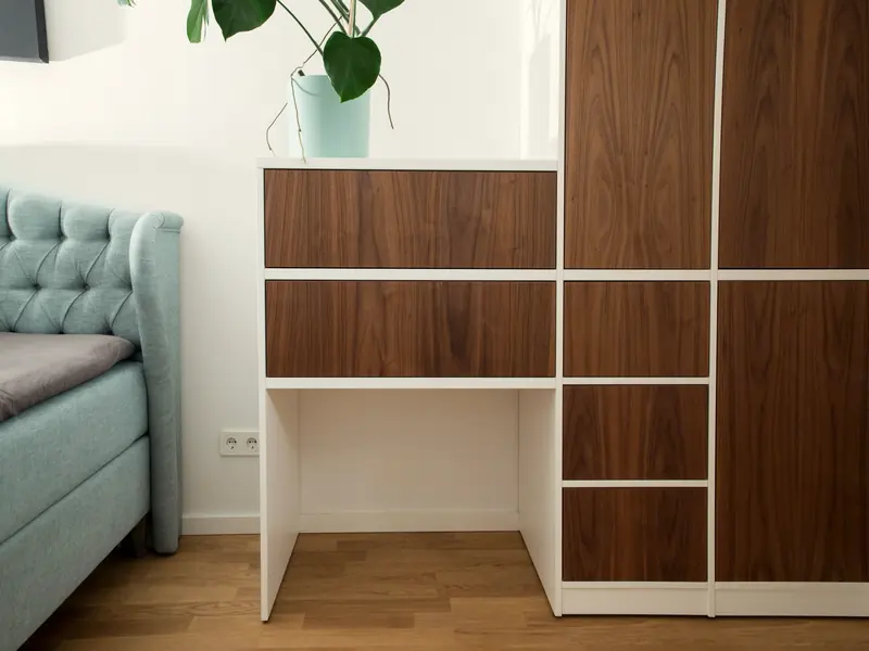 Schrankwand im Schlafzimmer mit Nussbaumfronten in weißem Rahmen und integriertem Schreibtisch neben dem Bett.