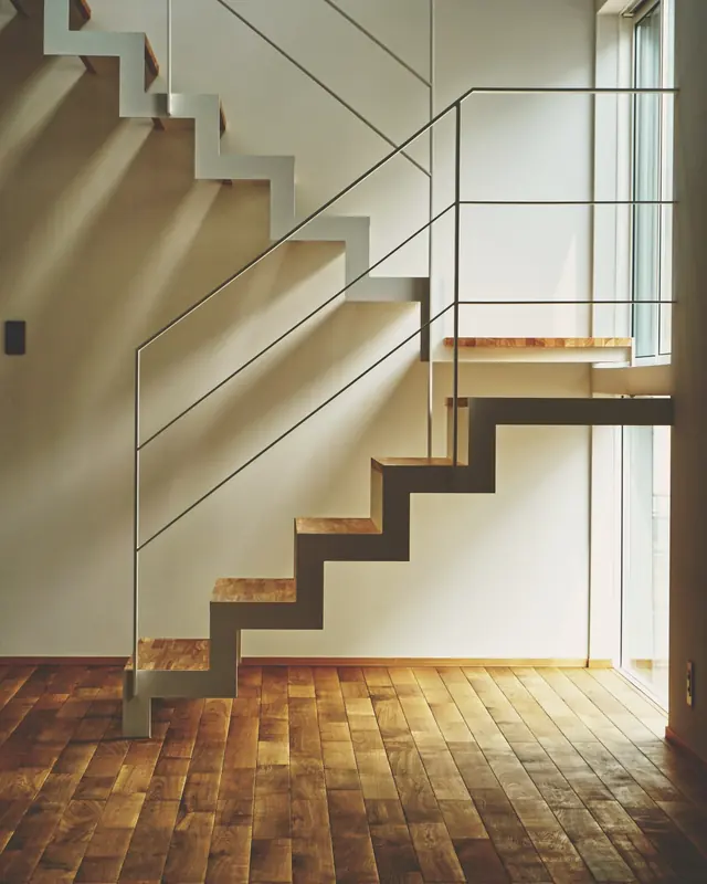 Treppe mit gefalteter Stahlwange und Eichenstufen vor einer hellen Wand, daneben ein filigranes Stabgeländer.
